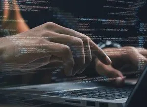 Hands typing on laptop with code overlay, suggesting software development or programming.