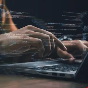 Hands typing on laptop with code overlay, suggesting software development or programming.