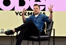 Man in denim shirt gestures while seated on stage at Vox Media event.