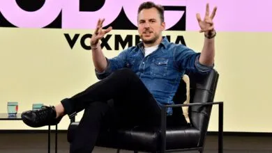 Man in denim shirt gestures while seated on stage at Vox Media event.