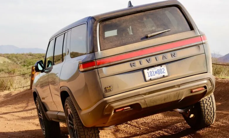 Rear view of a Rivian R1S SUV on a dirt road, slightly angled.