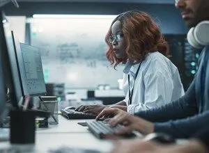 Two programmers working at computers in a modern office setting, focused on their screens.