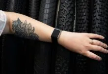 Arm with floral tattoo, fitness tracker, and ring against tire background.
