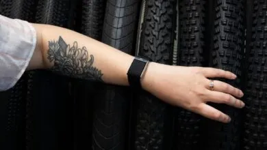 Arm with floral tattoo, fitness tracker, and ring against tire background.