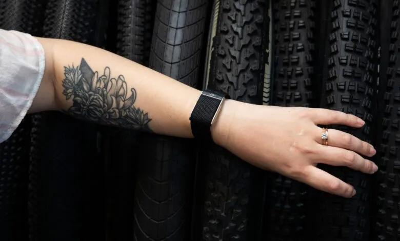 Arm with floral tattoo, fitness tracker, and ring against tire background.