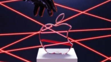 Apple logo on pedestal with red laser beams and gloved hand above.