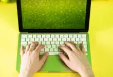 Lime green MacBook with hands typing on keyboard, vibrant yellow background.