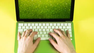 Lime green MacBook with hands typing on keyboard, vibrant yellow background.