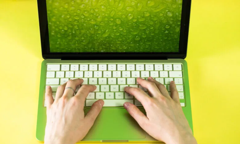Lime green MacBook with hands typing on keyboard, vibrant yellow background.