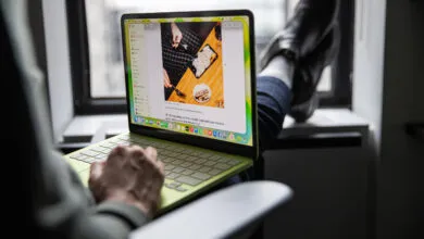 Person using a green MacBook laptop with feet up on a windowsill.