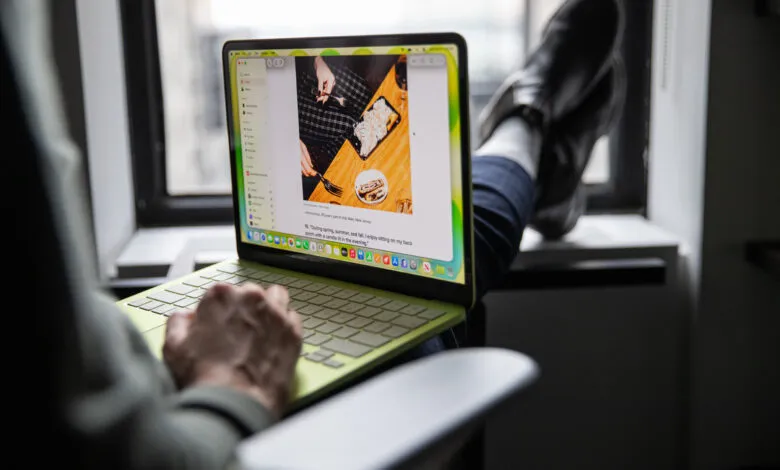 Person using a green MacBook laptop with feet up on a windowsill.