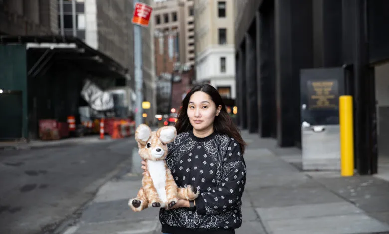 Woman holds deer plushie on city street, buildings in background.