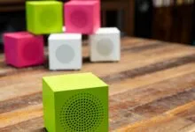Colorful cube speakers in green, pink, and white on a wooden table.
