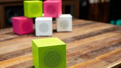Colorful cube speakers in green, pink, and white on a wooden table.