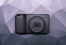 Black Ricoh GR camera centered on geometric background.