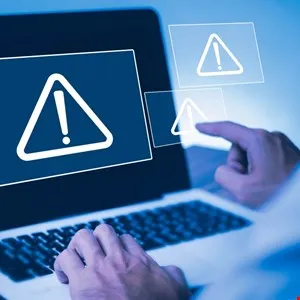 Laptop screen displays a warning symbol with exclamation point, user interacts with floating icons.