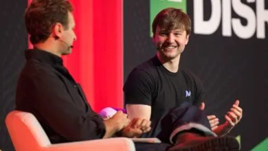 Two men on stage at a conference, one smiling and gesturing.