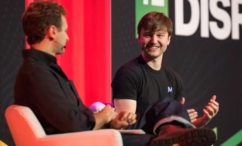 Two men on stage at a conference, one smiling and gesturing.