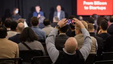 Audience member records panel discussion with smartphone at conference.