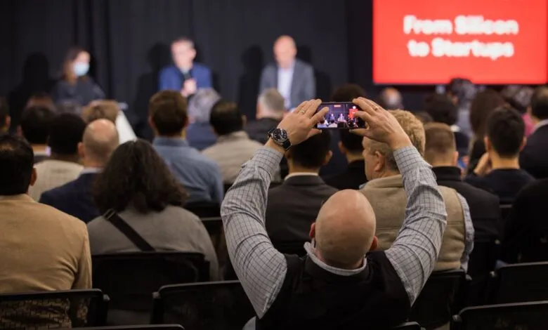 Audience member records panel discussion with smartphone at conference.