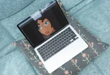 Laptop on floral pillow displays digital art of a woman's face.
