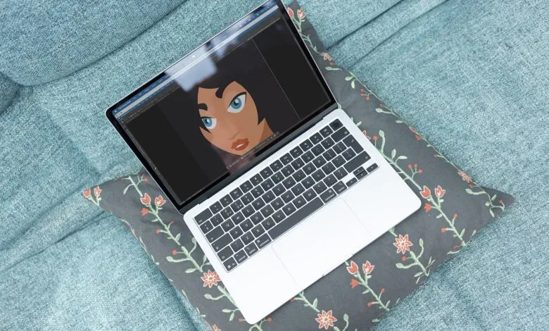 Laptop on floral pillow displays digital art of a woman's face.