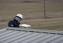 Technician in hard hat installs antenna on metal roof.
