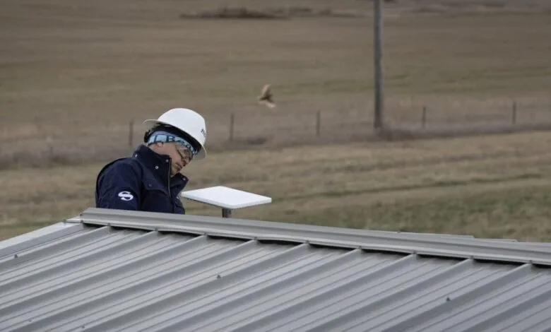 Technician in hard hat installs antenna on metal roof.