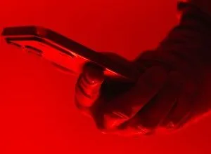 Hand holding a smartphone illuminated by a strong red light source.