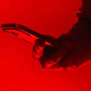 Hand holding a smartphone illuminated by a strong red light source.