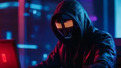 Person in hoodie and glowing mask sits at laptop in neon-lit room.