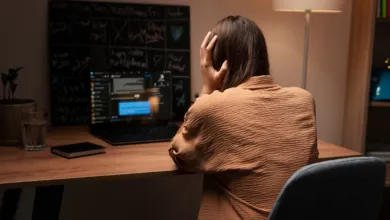 Woman with head in hands sits at desk with laptop, looking stressed.