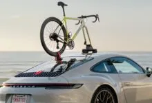 A bicycle is mounted on the back of a silver Porsche using a suction rack.