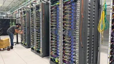 Technician works on servers in a data center, rows of racks with colorful cables.