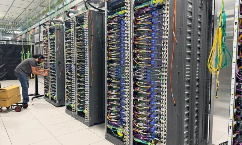 Technician works on servers in a data center, rows of racks with colorful cables.