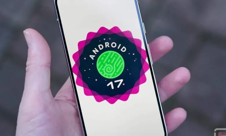 Hand holding phone displaying Android 17 logo on a light background.