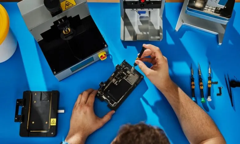 Person repairing an iPhone with specialized tools on a blue surface.