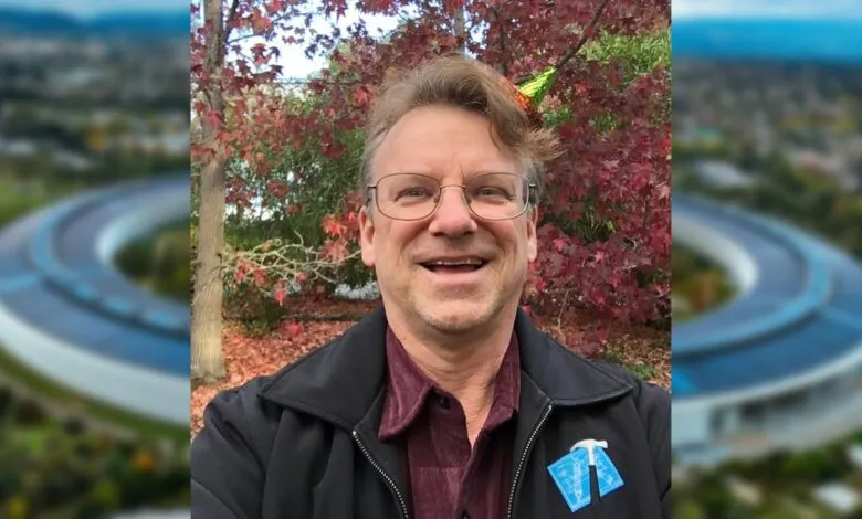 Man smiles in front of Apple Park, wearing glasses and a black jacket.