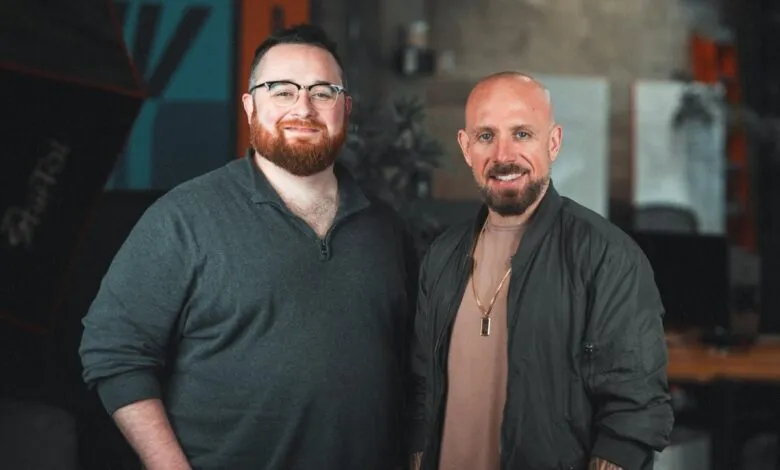 Two smiling men pose indoors with soft, diffused lighting.