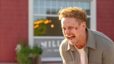 Man with a bruise on his face is laughing outdoors.