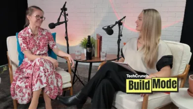 Two women sit in chairs for a podcast recording, smiling at each other.