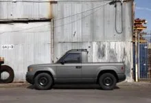 Gray pickup truck parked against corrugated metal wall.