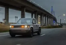 Slate truck driving on road with bridge in background.