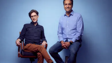 Two men, Brett and Ash, sit against a blue backdrop in a studio portrait.
