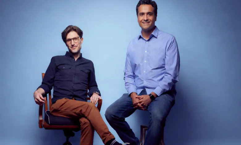 Two men, Brett and Ash, sit against a blue backdrop in a studio portrait.