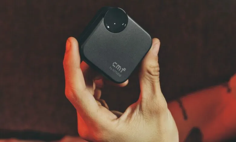 Hand holding dark grey CMF Buds 2a charging case with circular detail.