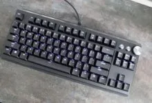 Black mechanical keyboard with purple backlight on a gray textured surface.