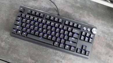 Black mechanical keyboard with purple backlight on a gray textured surface.