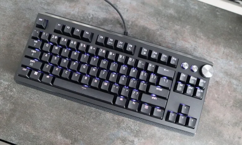 Black mechanical keyboard with purple backlight on a gray textured surface.