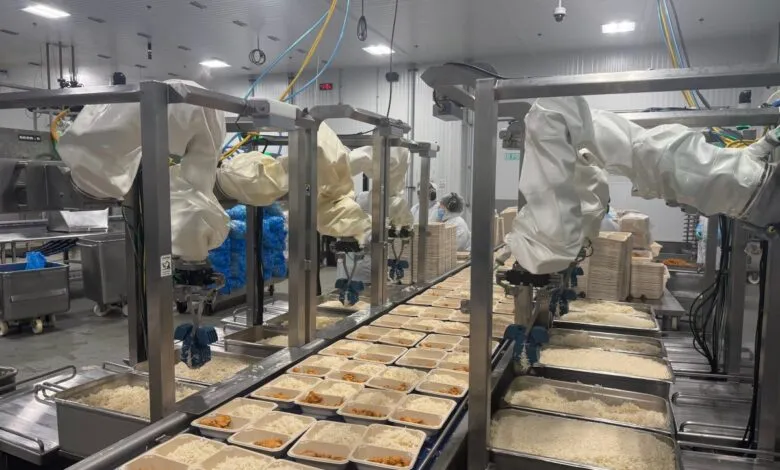 Automated food production line with robots filling meal containers with rice.